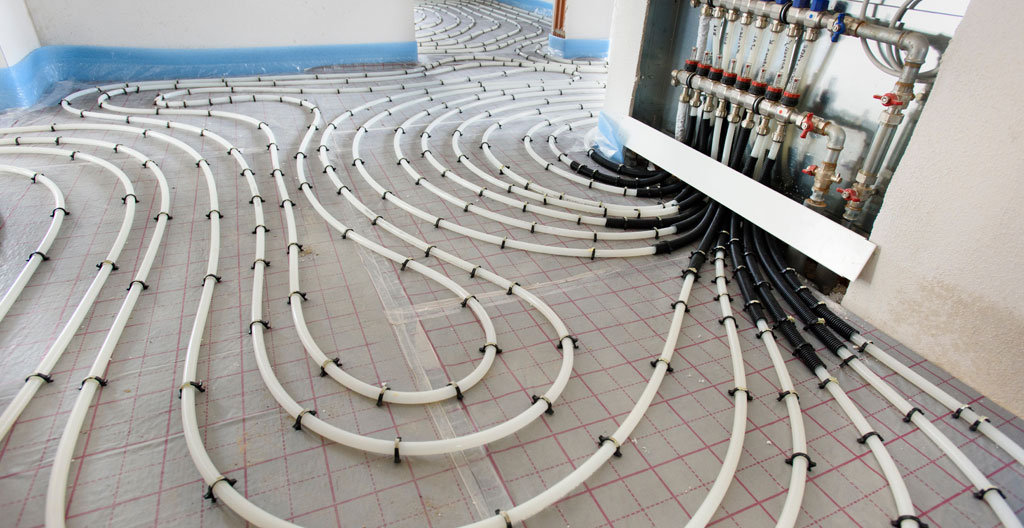 Gros plan sur tubes PER orange en serpentin posés sur panneau isolant pour plancher chauffant hydraulique